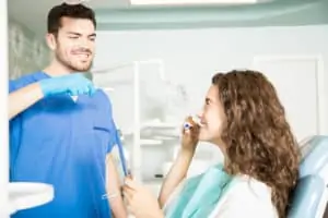 Dentist showing technique of brushing teeth to his female patient in dental clinic